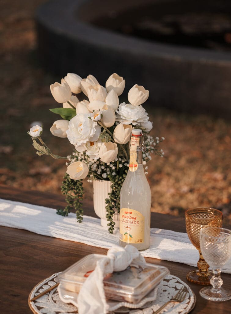 Close-up detail of white floral arrangement and sparkling lemonade at Raleigh Rose Garden proposal picnic table.