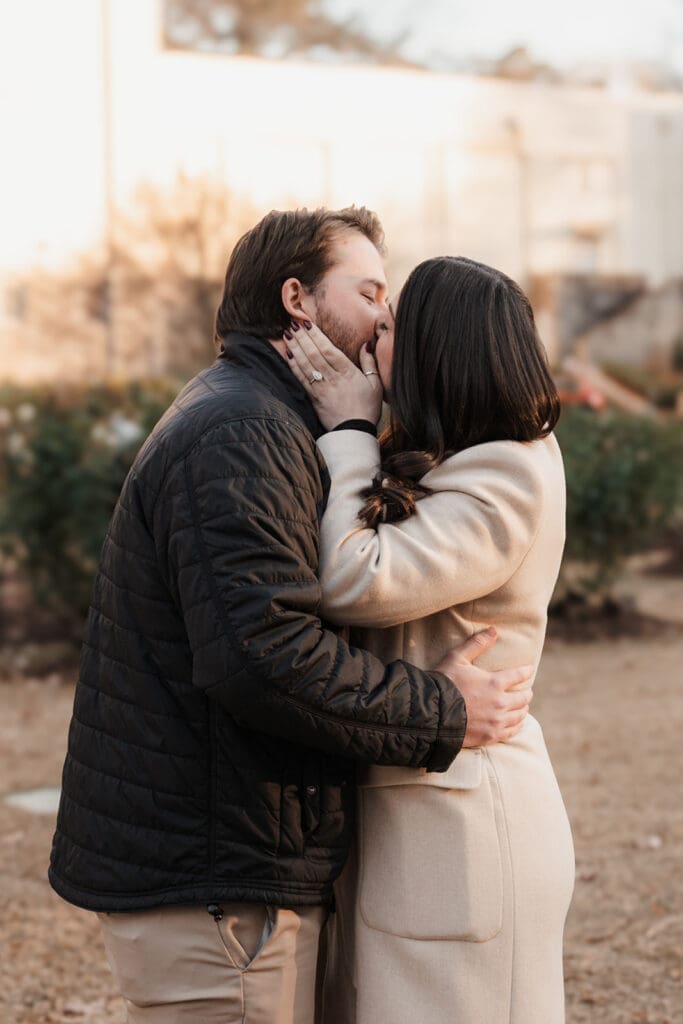 Newly engaged couple hugging at Raleigh Rose Garden after surprise proposal.