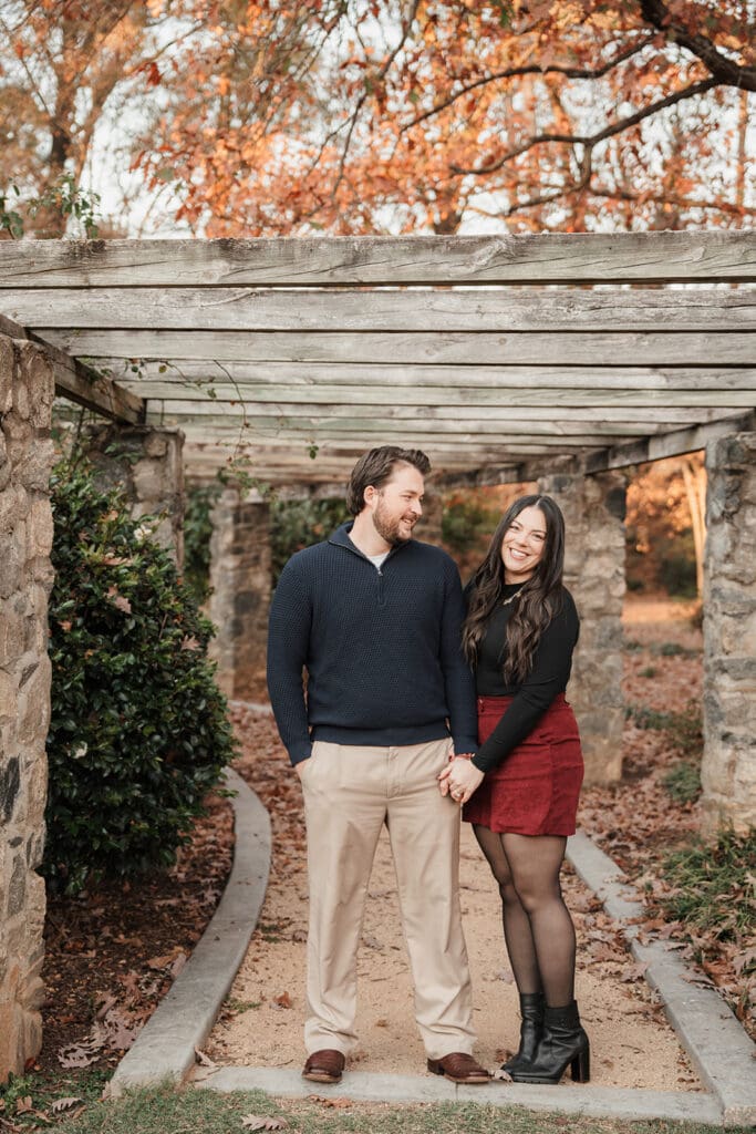 Couple standing beneath pergola at Raleigh Rose Garden after surprise proposal.
