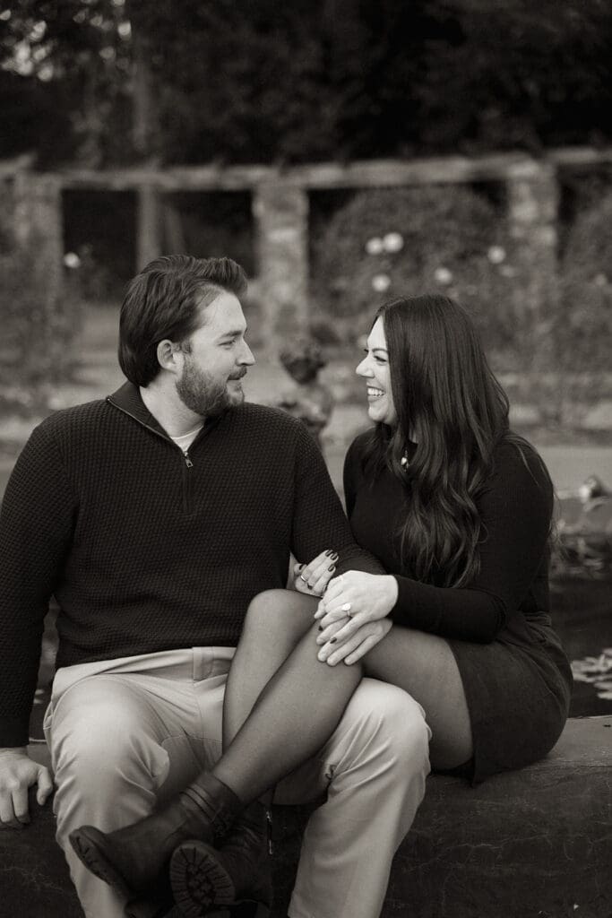 Black and white engagement portrait of couple seated at Raleigh Rose Garden.