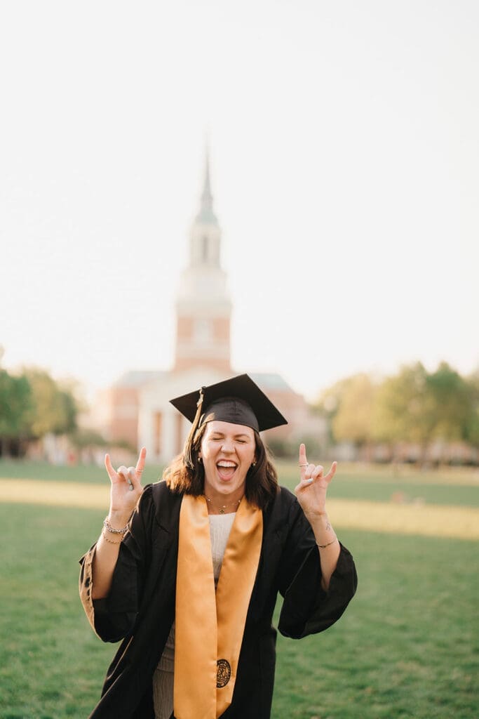 Wake Forest graduate celebrating on campus lawn wearing cap and gown during senior photo session