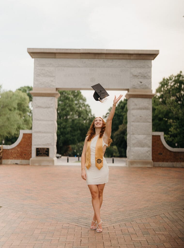 Wake Forest graduate celebrating with champagne near campus archway in Winston-Salem