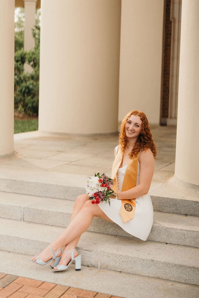 Wake Forest graduate seated on steps of Wait Chapel holding bouquet during editorial graduation photos