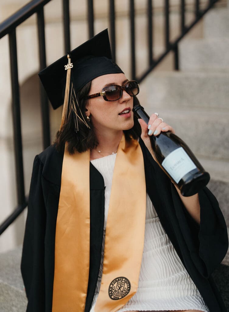 Editorial Wake Forest graduation portrait of senior wearing cap and gown with champagne on campus steps