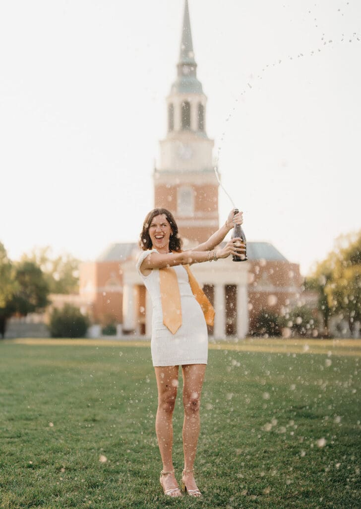 Wake Forest senior popping champagne on campus lawn with Wait Chapel in the background
