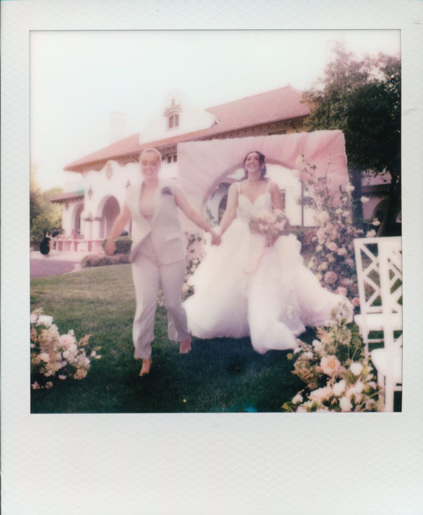 Instant film photo of newlyweds running through a floral ceremony setup.