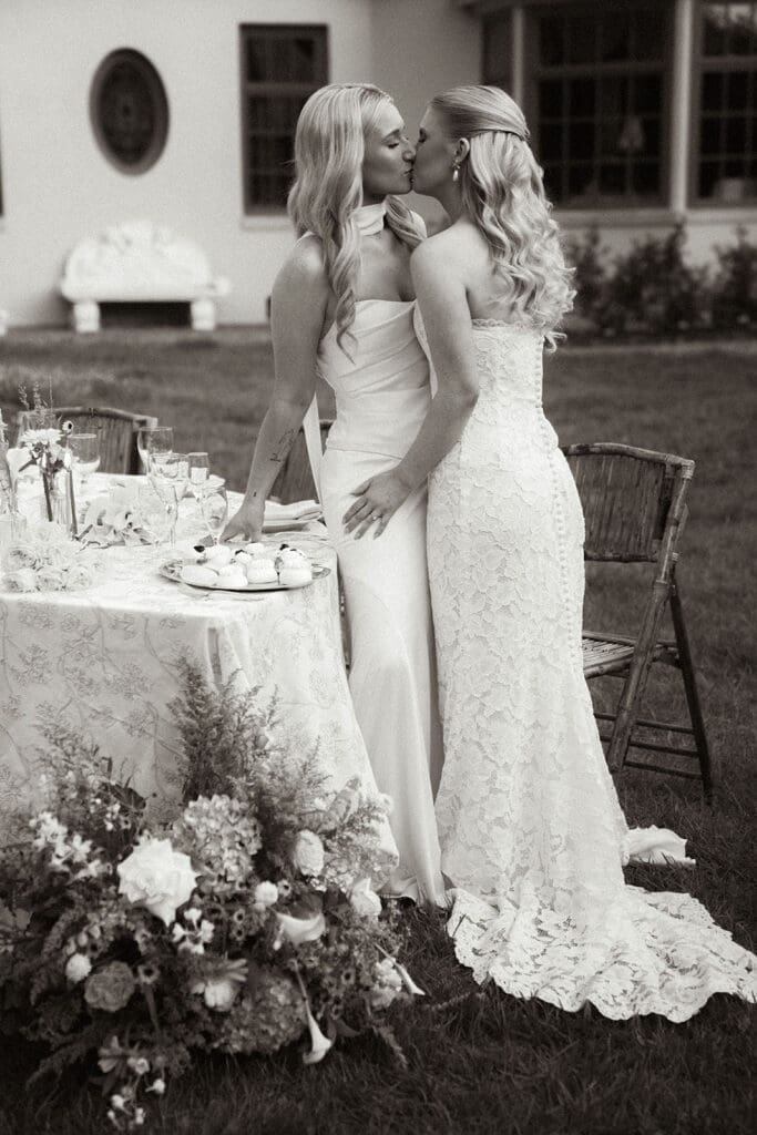 Editorial wedding portrait of two brides beside the reception tables.