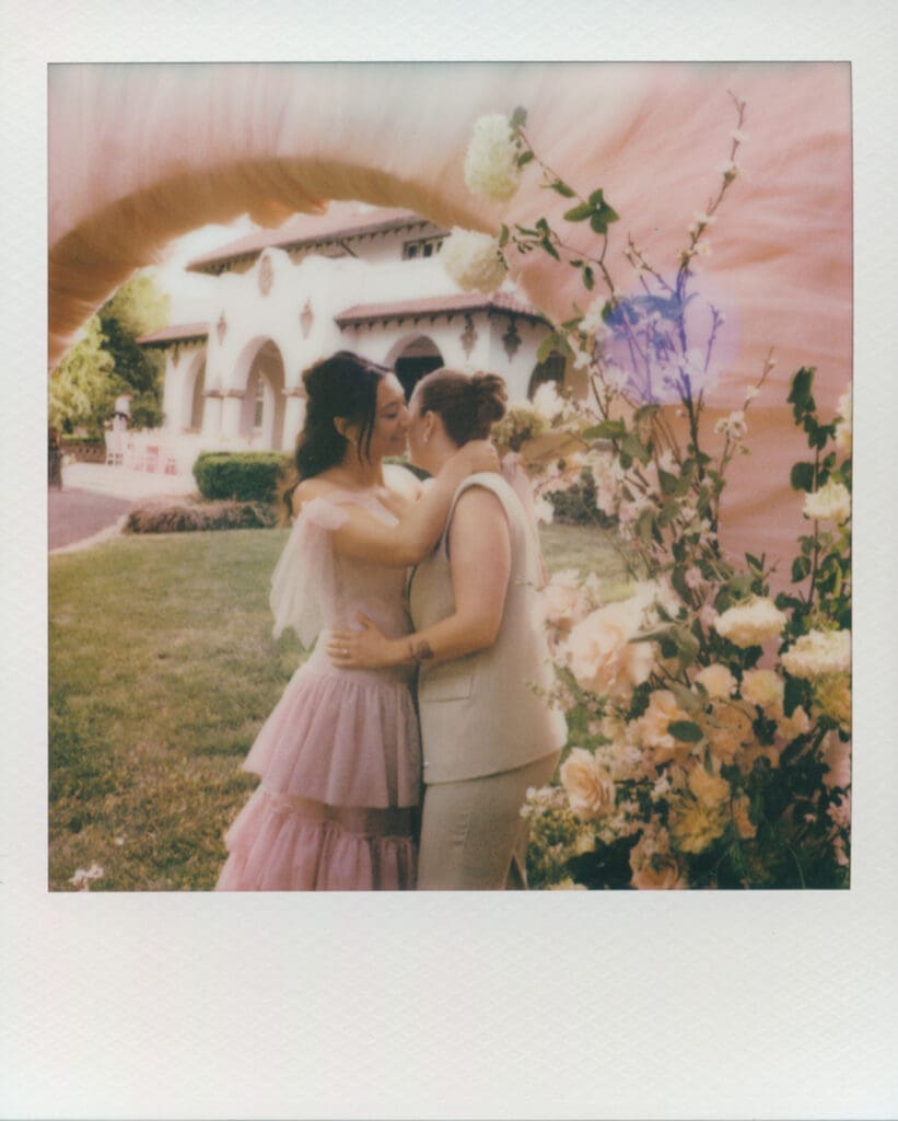 Instant film portrait of a couple embracing beneath a floral ceremony installation.