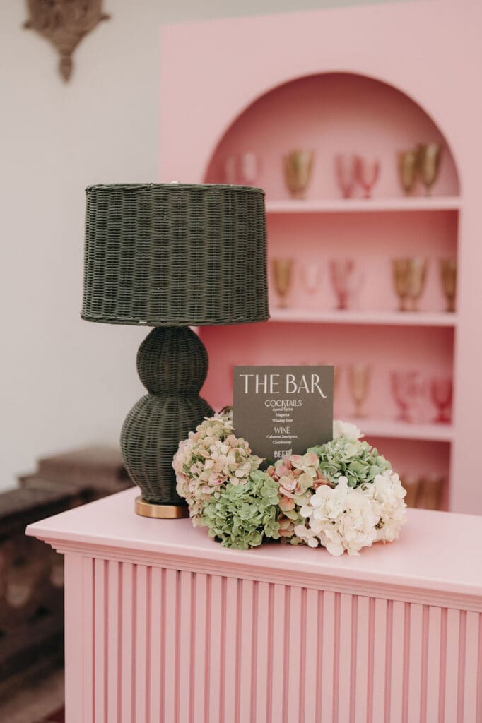Wedding bar details with blush shelving, florals, and signature cocktail menu.