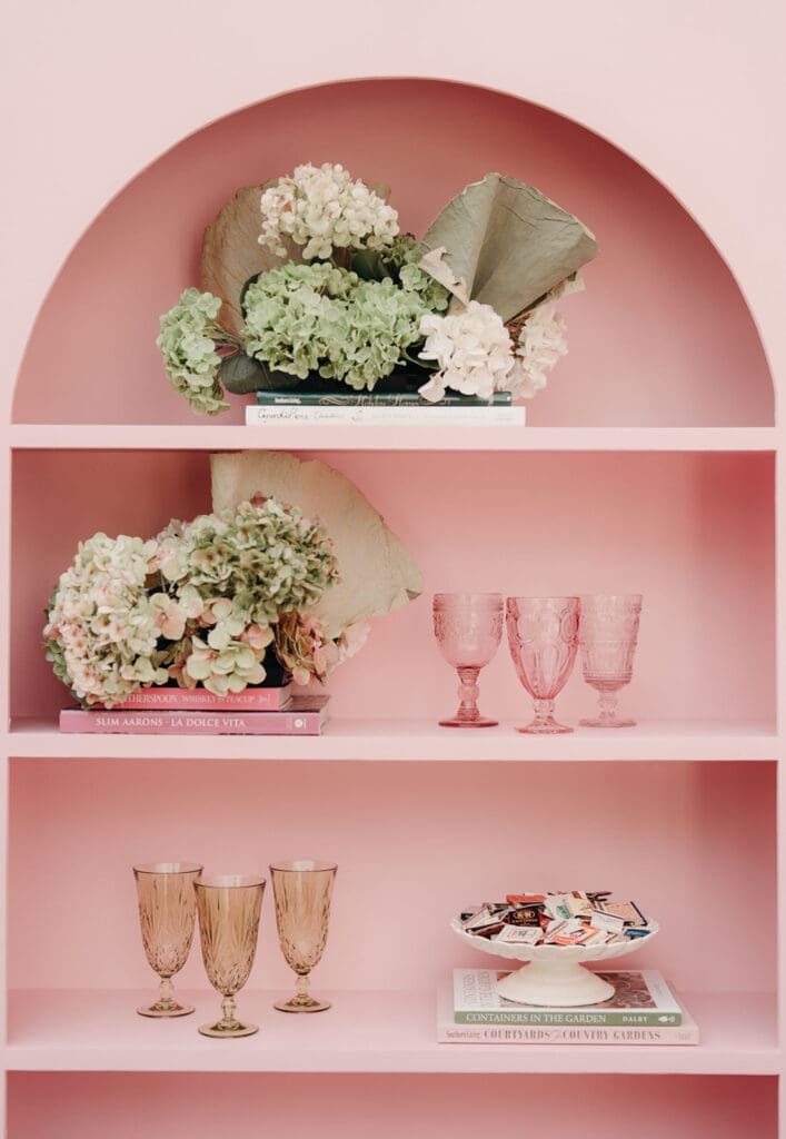 Wedding bar styling with pink shelves, vintage glassware, and floral arrangements.