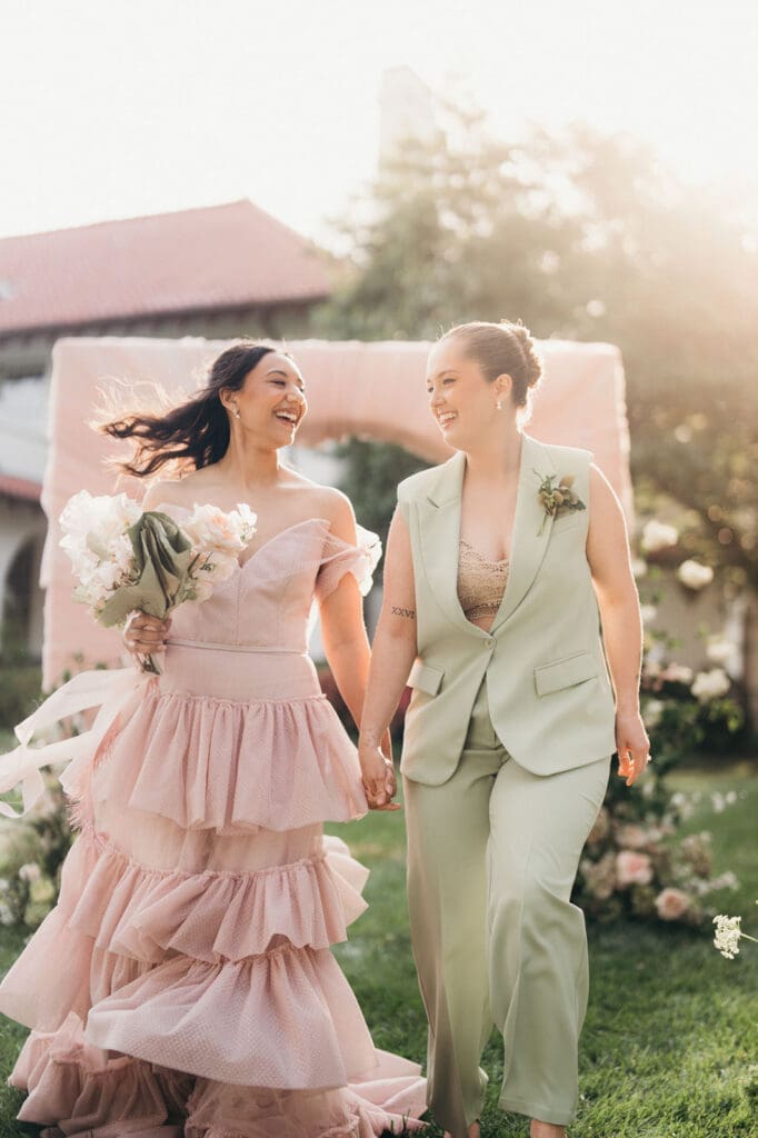 Couple walking hand in hand beneath a floral ceremony arch during a Hill House wedding editorial.