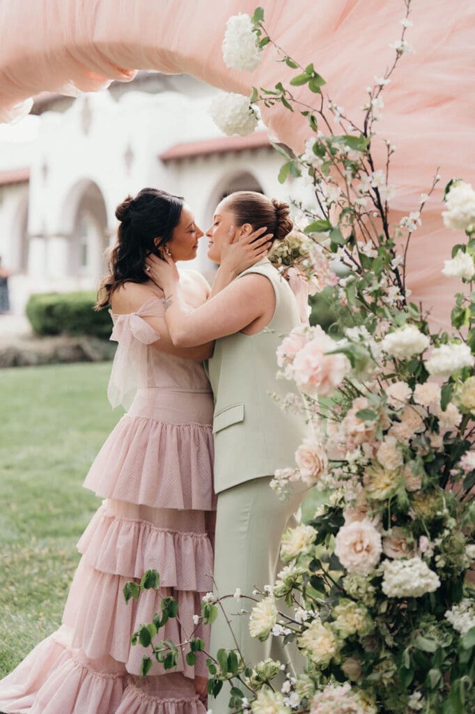 Romantic wedding portrait beneath a blush floral ceremony arch.