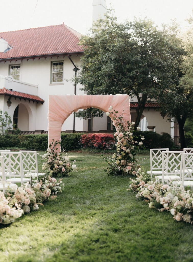 Blush fabric ceremony arch with lush garden florals at Hill House.