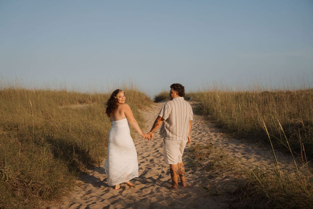 Couple walking away on sand dunes holding hands.