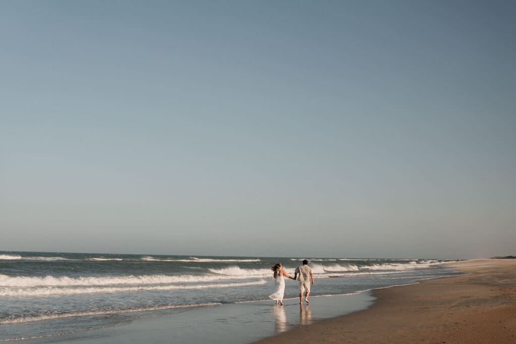 Couple walking away on avon beach with ocean to their left,