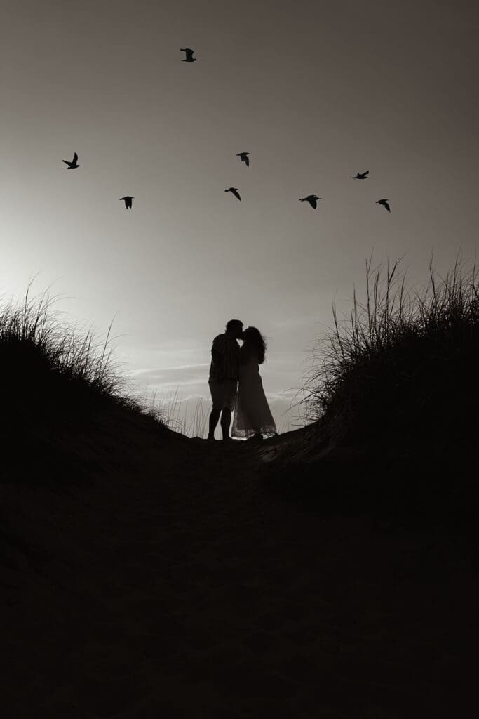 silhouette if couple kissing on avon beach with seagulls flying over.